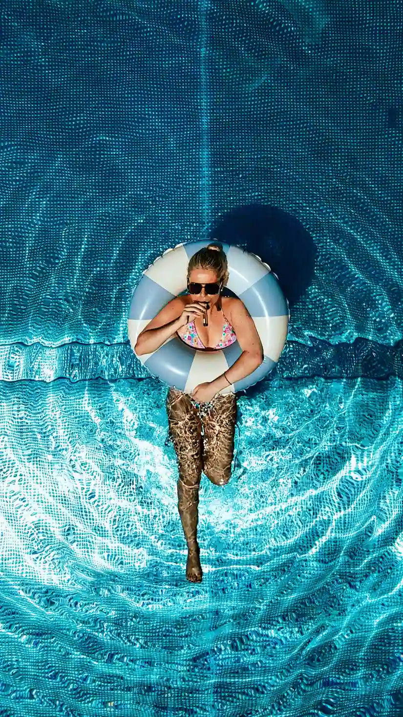 Frau entspannt in einem Schwimmreifen im Pool, von oben betrachtet. Sie trinkt CLARITY Liquid Rootshot.